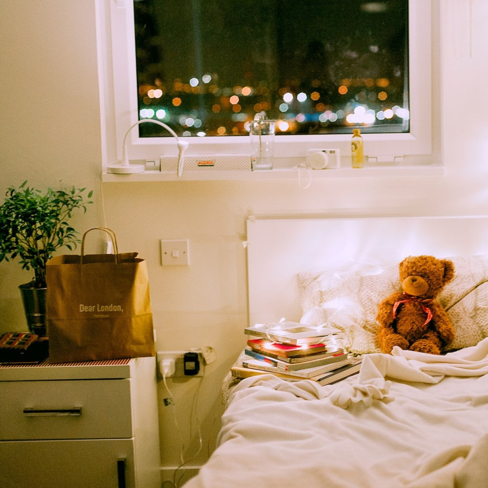 a small bedroom with fairy lights and a teddy bear
