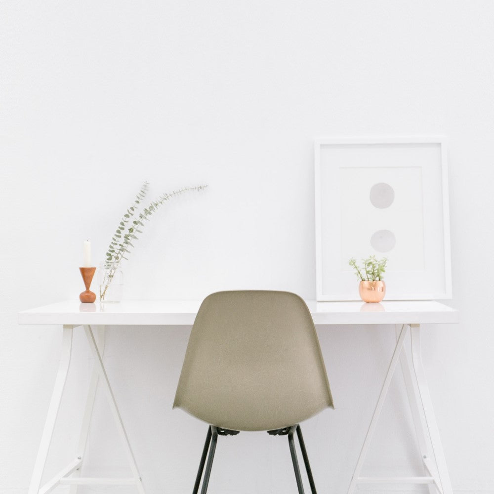 A minimalist home office set up of a white desk and grey chair against a white wall